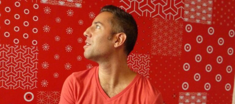 Vibrant red background with festive geometric and snowflake patterns, featuring a smiling man in a red T-shirt, creating a cheerful holiday atmosphere.